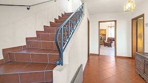 Eine Treppe mit braunen Fliesen und einem Metallgeländer, die zu einem Raum mit Heizkörper und Holzschrank führt.