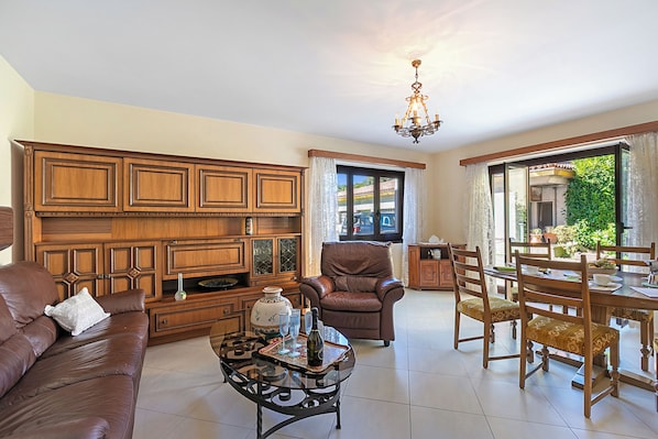 A spacious living room with a brown leather sofa, a wooden cabinet, a dining table with chairs, and a chandelier. - Casa Ana 1 with Garden & Parking for 3, Losone, Switzerland (Losone)
