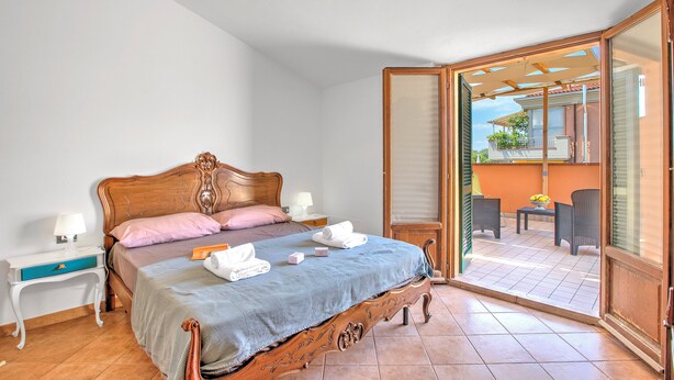 Ein Schlafzimmer mit einem hölzernen Bett, einem Nachttisch, einer Lampe und Blick auf den Außenbalkon.
