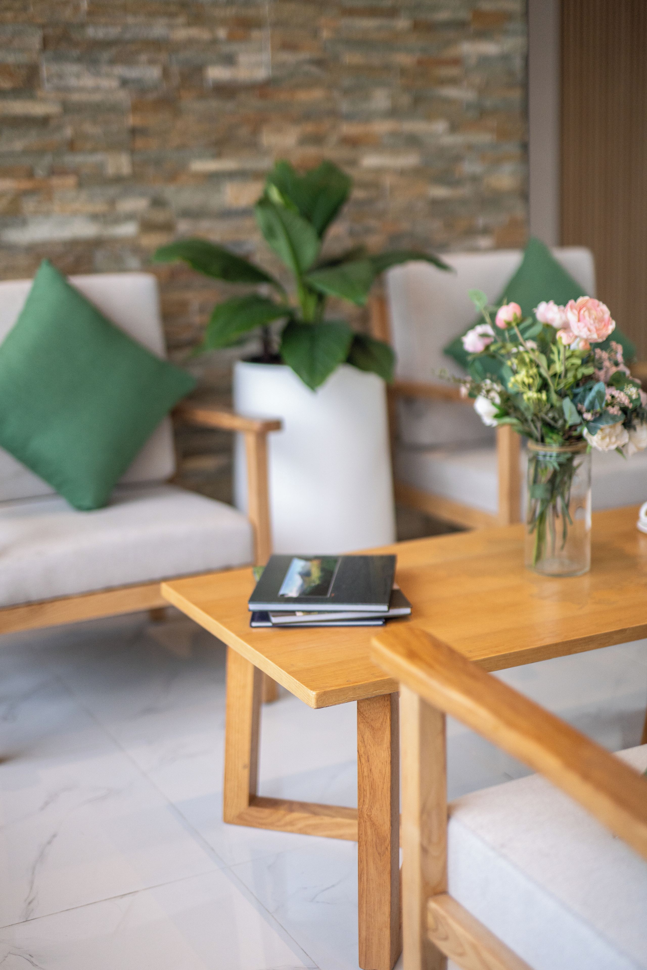 A wooden table with a book, a potted plant, and a vase with flowers.