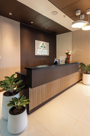 A hotel reception desk with a logo, a digital screen, and potted plants. - Sage Hotel by SMS Hospitality (Oroquieta)