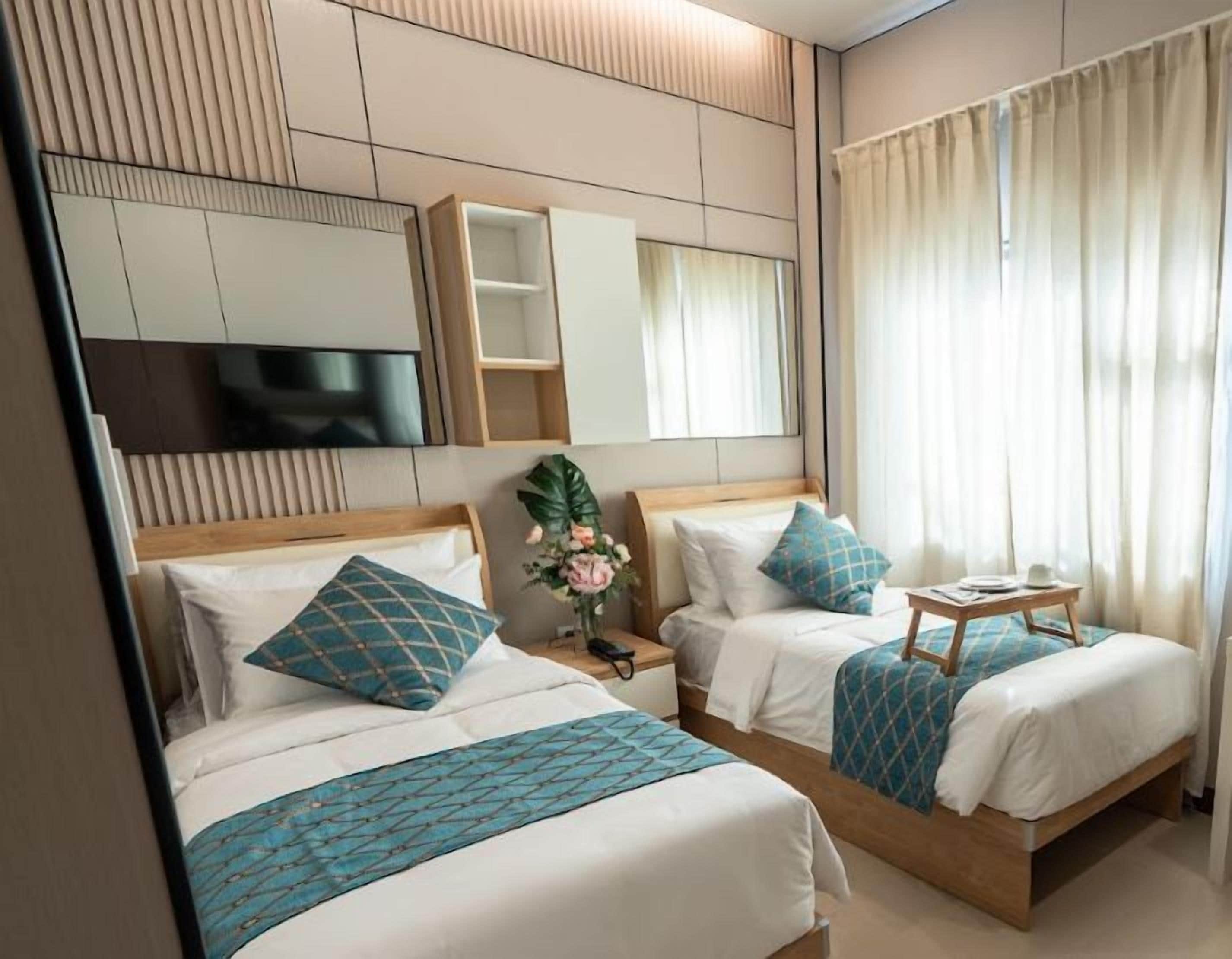 A hotel room with two beds, a TV, a small table, and a window with curtains.