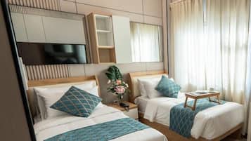 A hotel room with two beds, a TV, a small table, and a window with curtains.