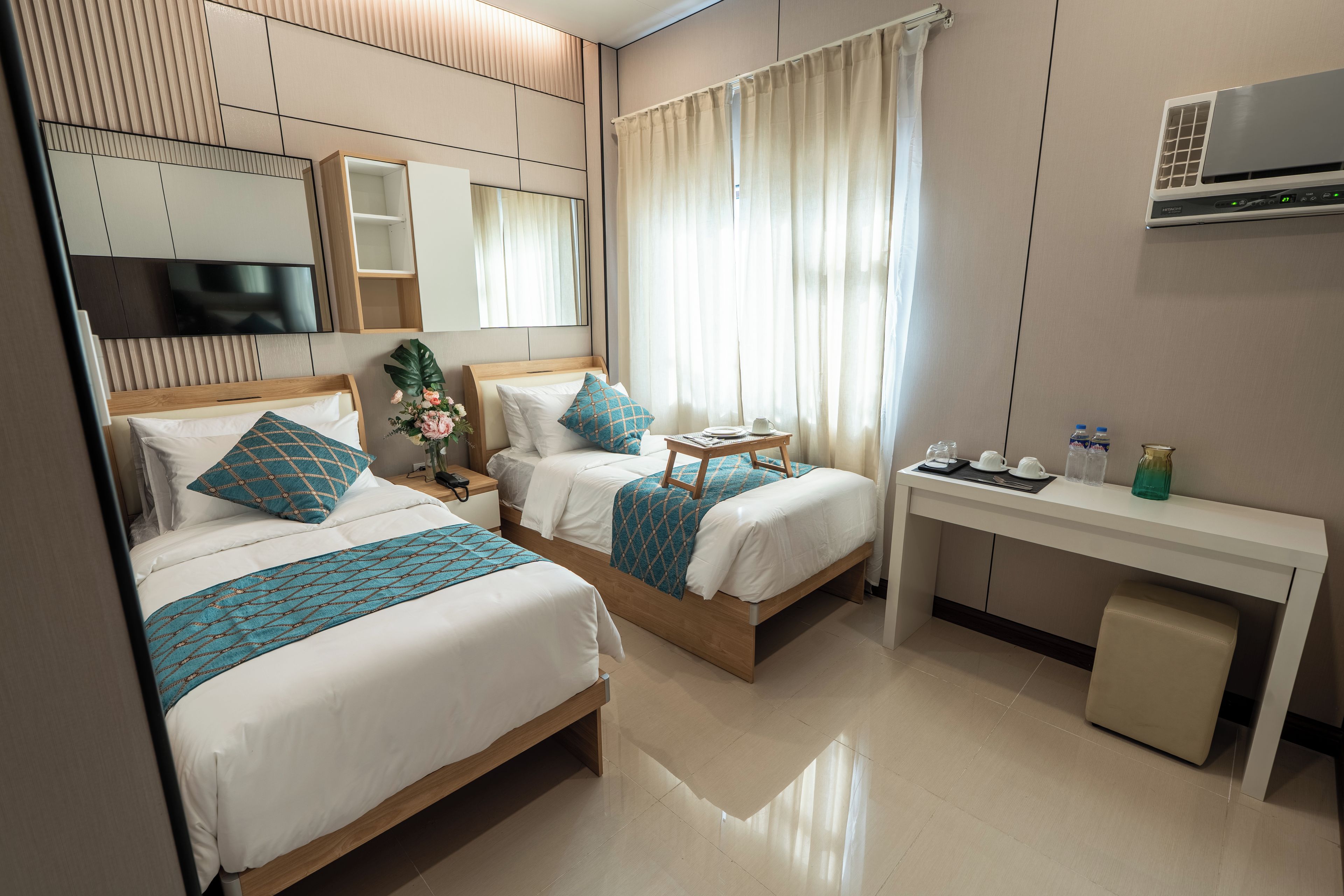A hotel room with two beds, a desk, and a TV.