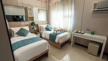 A hotel room with two beds, a desk, and a TV.