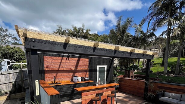 A wooden deck with a hot tub, a bar area with stools, and a pergola overhead. - La Maison Soleil with heated Swim Spa (Waiheke Island)