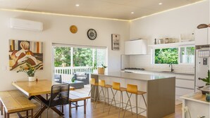 A modern kitchen with a central island, bar stools, and a dining area with a bench and chairs. - La Maison Soleil with heated Swim Spa (Waiheke Island)