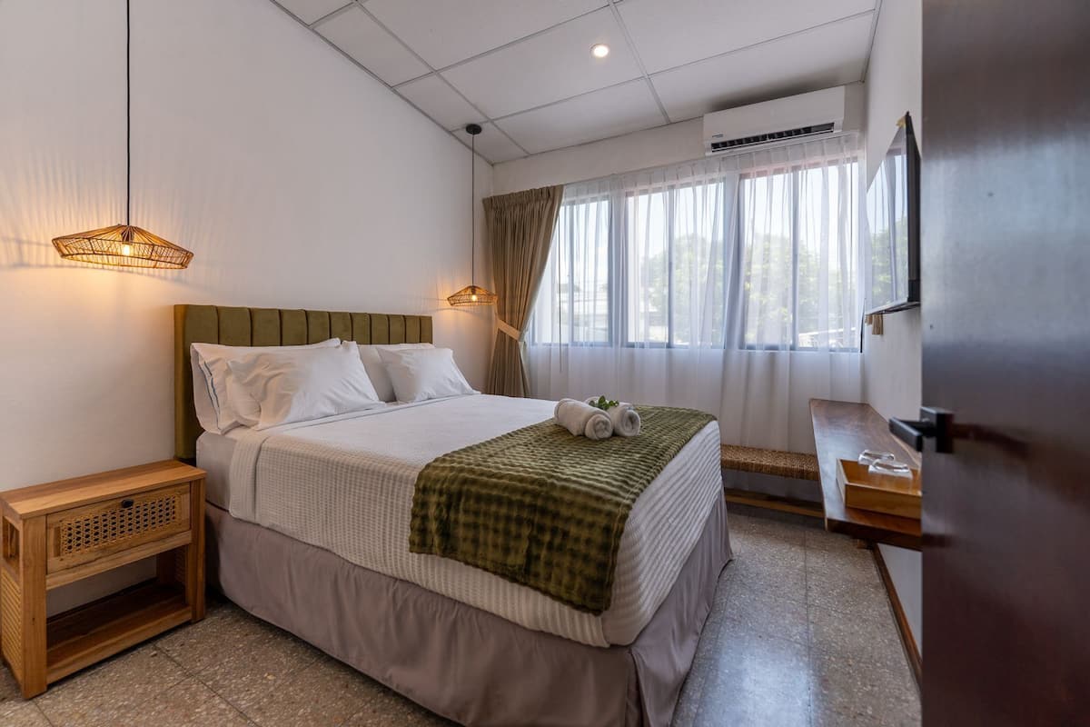 Une chambre bien rangée, avec un lit, des tables de chevet, un banc et une fenêtre avec des rideaux.