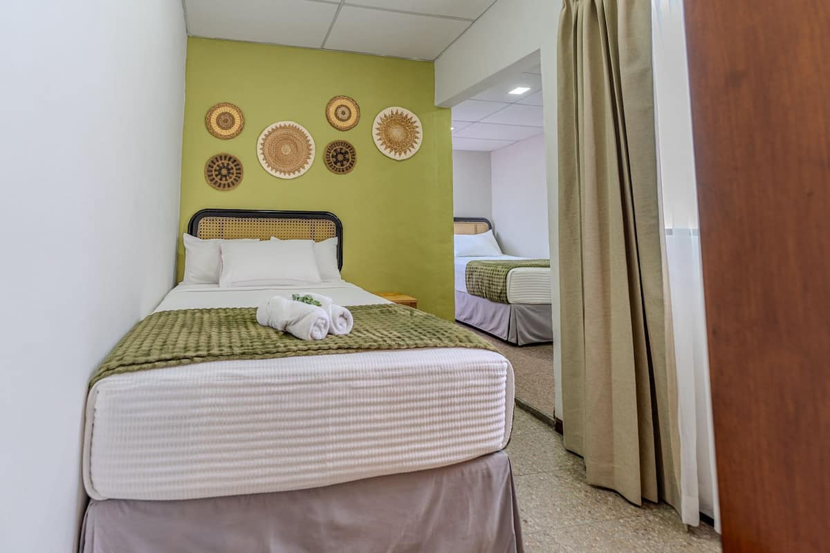 Une chambre d’hôtel avec deux lits, un mur d’accent vert et des œuvres d’art décoratives.