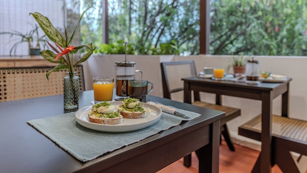 A breakfast table with a plate of toast, a vase with a plant, a coffee maker, and a glass of orange juice. - Casa Lúmina - Hotel Boutique y Spa (San Salvador)