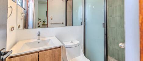 A modern bathroom with a white sink, toilet, and glass shower enclosure.