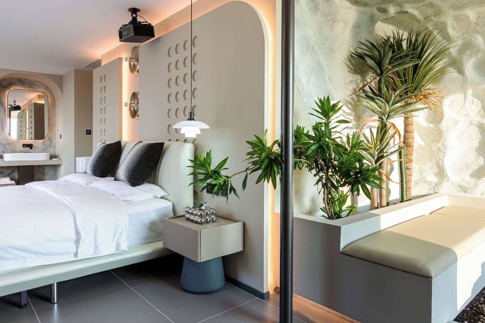 A modern bedroom with a bed, bedside table, lamp, and a wall-mounted shelf with plants.