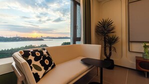 Ein modernes Wohnzimmer mit einer Couch, einem kleinen Tisch und einem großen Fenster mit Blick auf einen Fluss und den Stadtpanoramahimmel.