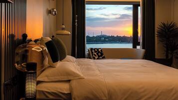 Una camera d'albergo con un letto grande, vista su un tramonto sull'acqua e uno skyline sullo sfondo.