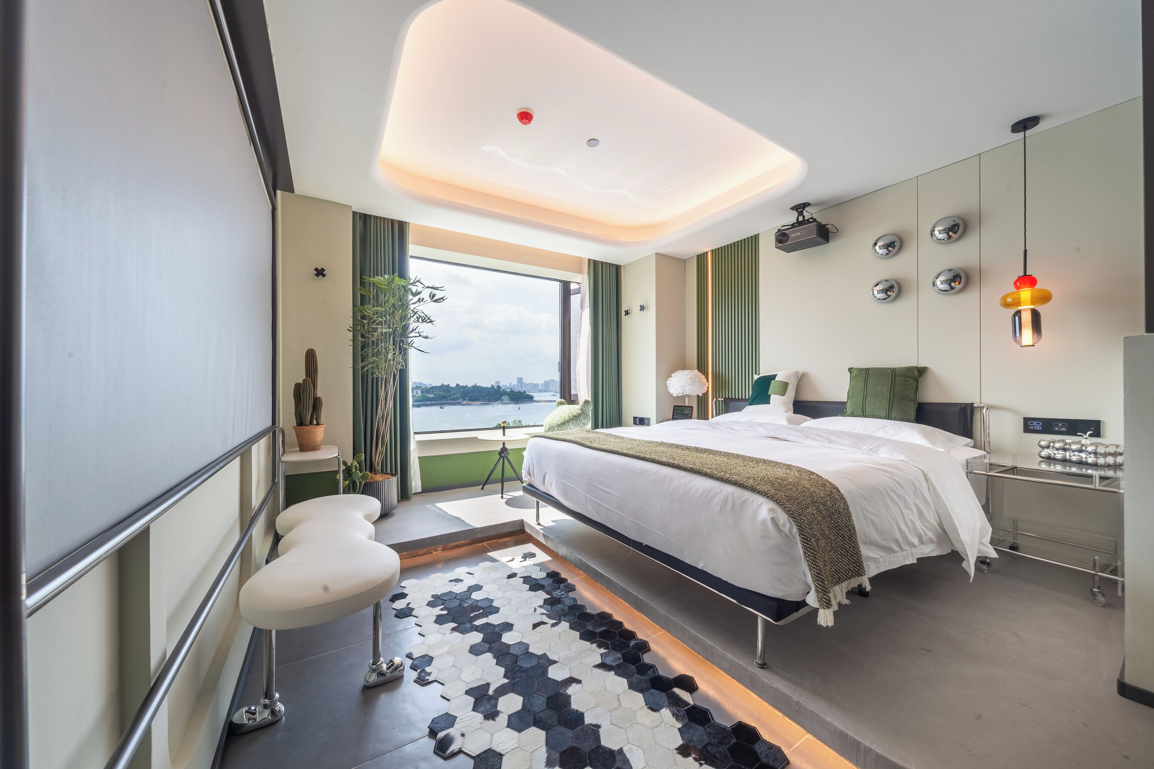 Ein modernes Hotelzimmer mit einem großen Bett, Blick auf die Stadt, einem Schreibtisch mit Lampe und einem einzigartigen sechseckigen Teppich.