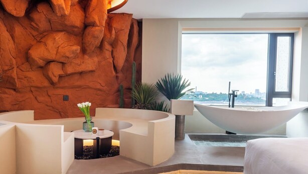 Ein modernes Hotelzimmer mit einer gebogenen Sitzecke, einer großzügigen Badewanne und Blick auf die Stadt durch das Fenster.