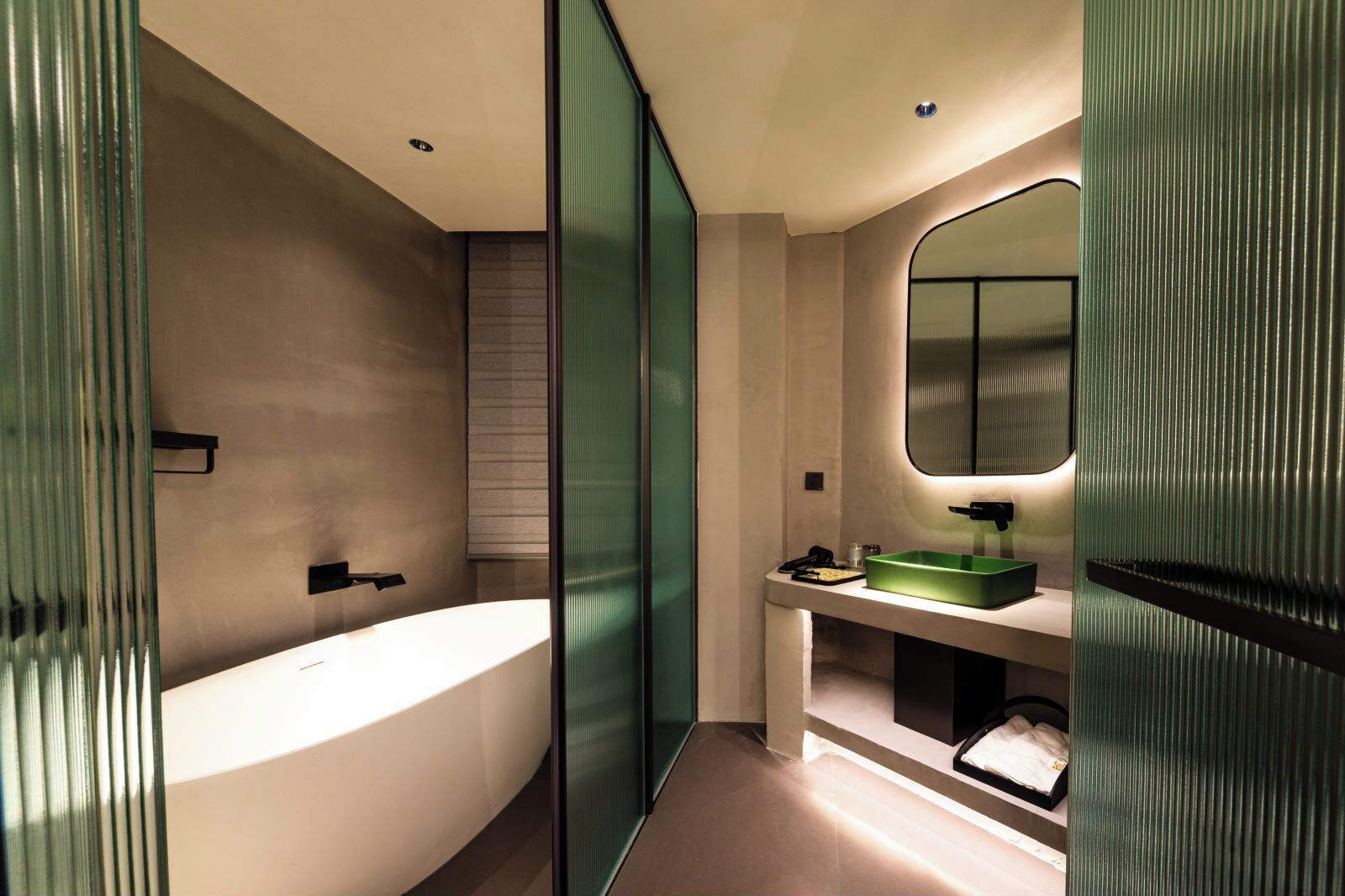 A modern bathroom with a freestanding bathtub, a green sink, and a large mirror.