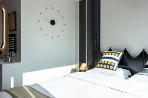 Un dormitorio moderno con un reloj de pared grande, una cama con ropa de cama blanca y un cabecero negro.