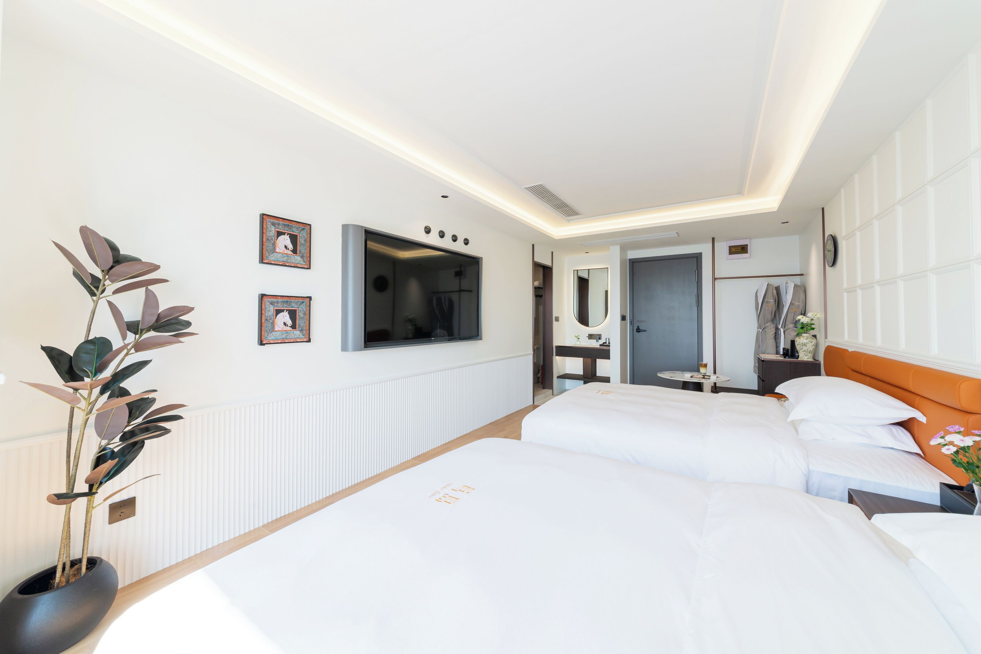 A hotel room with two beds, a TV, a plant, and a bathroom visible through an open door.