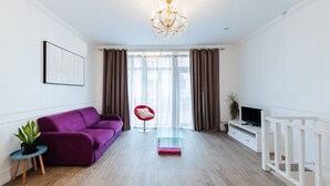 Un soggiorno moderno con un divano viola, una poltrona rossa, un tavolino in vetro e un mobile porta TV.