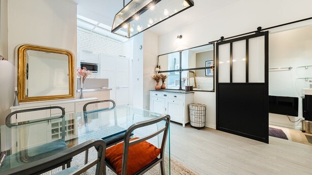Una cucina moderna con mobili bianchi, un tavolo da pranzo in vetro e una porta scorrevole nera.