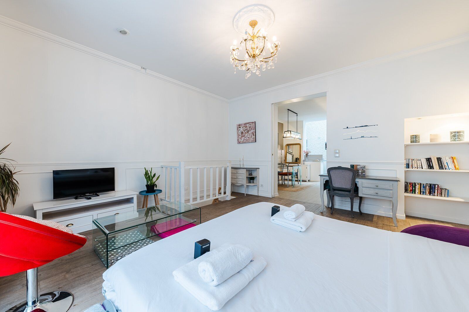 Una habitación de hotel con una cama grande, un escritorio, un televisor, una estantería y una silla roja.