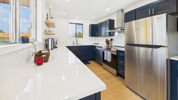 Una cocina moderna con armarios azul oscuro, electrodomésticos de acero inoxidable y encimera blanca.