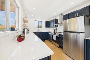 Una cocina moderna con armarios azul oscuro, electrodomésticos de acero inoxidable y encimera blanca.