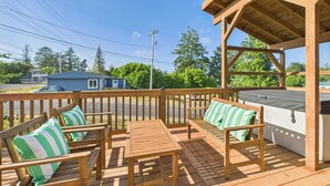 Una terraza de madera con mobiliario exterior, incluyendo sillas y una mesa, además de un área cubierta con una parrilla.