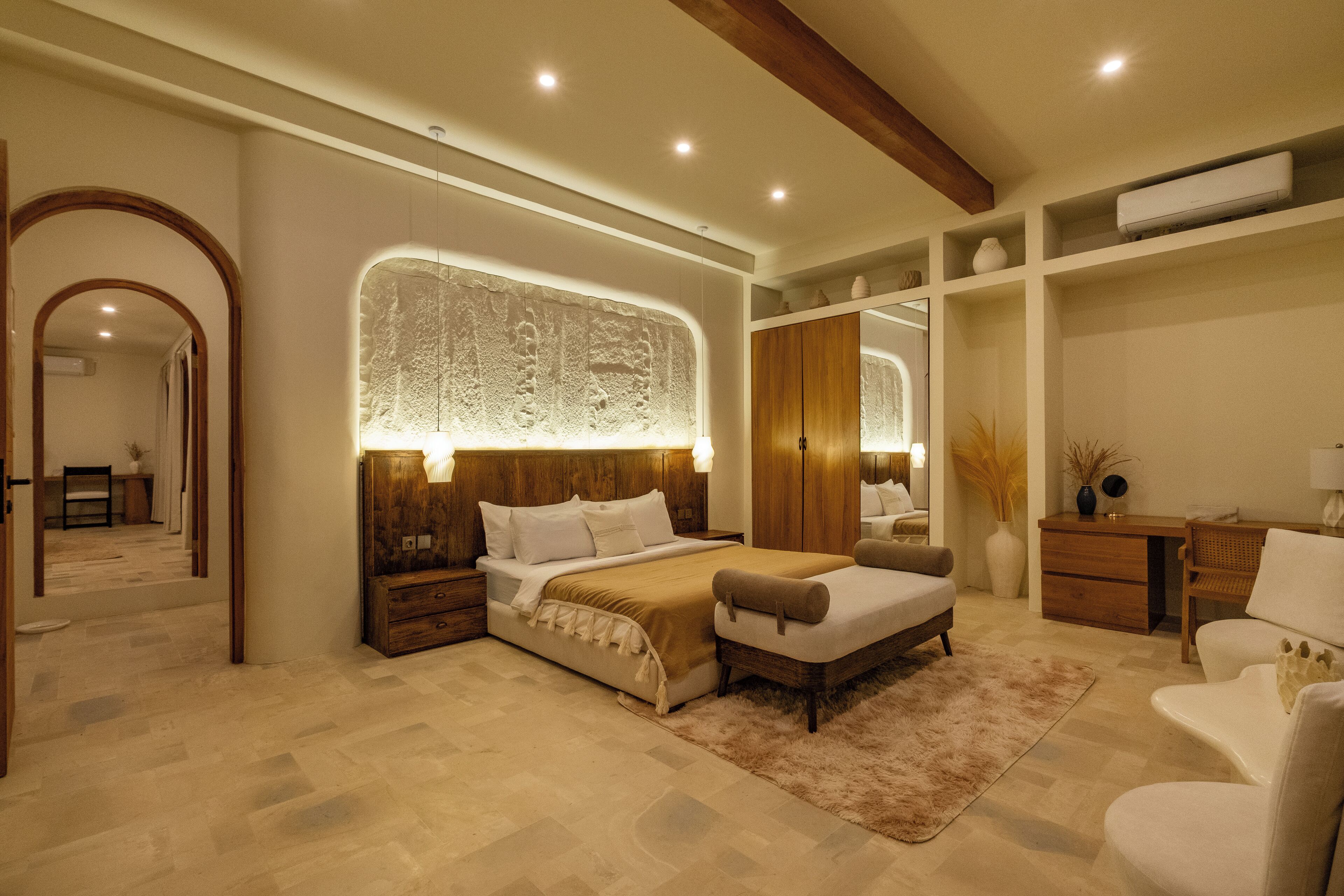 A spacious bedroom with a large bed, a nightstand, a dresser, and a seating area with a chair and a small table.