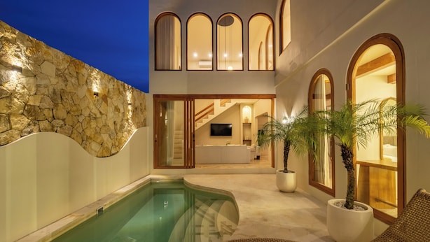A pool area with a stone wall, a lounge chair, and a potted palm tree. - 3BR Luxe Pool Villa Anaya (Canggu)