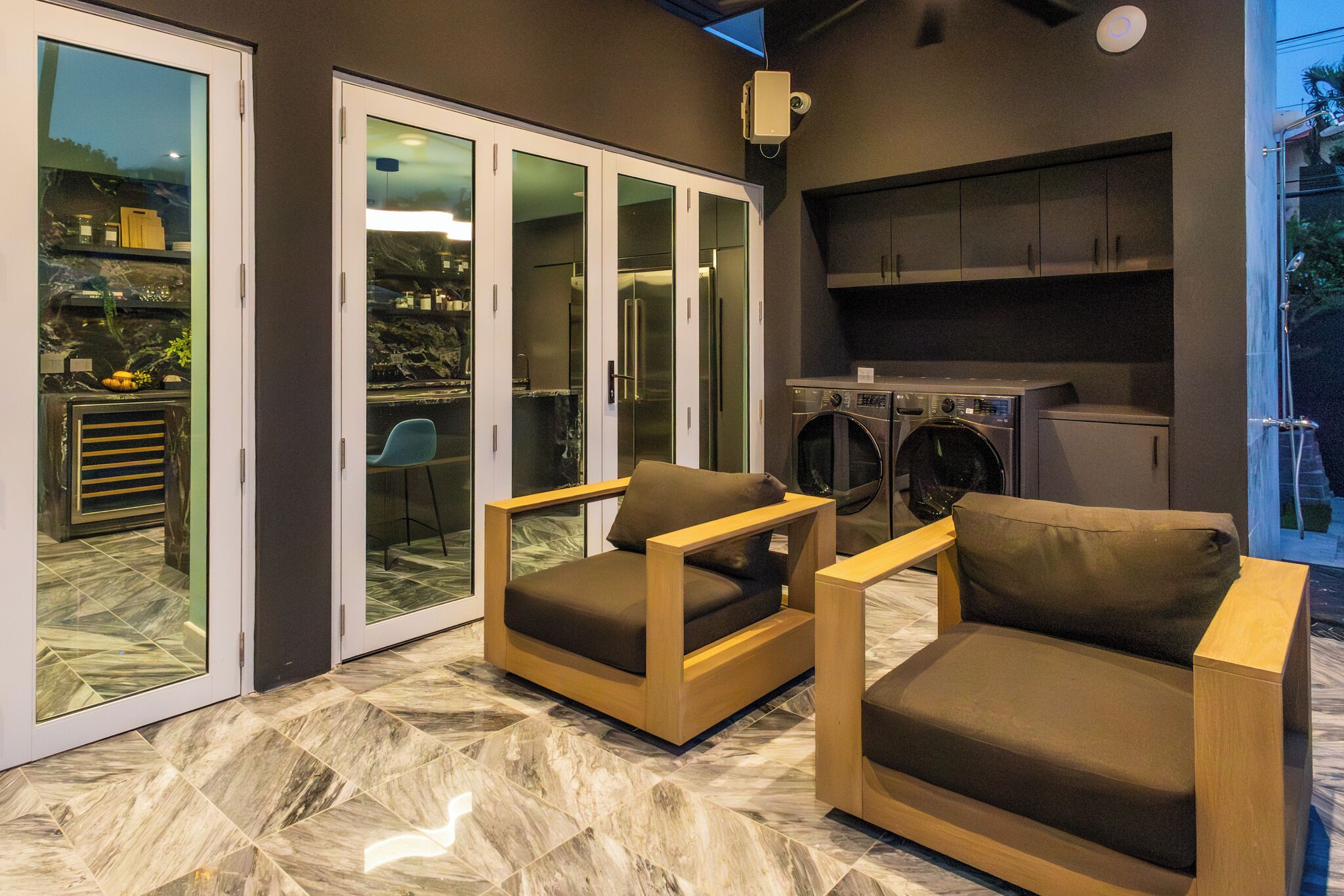 Una cocina moderna con lavadora incorporada, puerta corrediza de vidrio que da a un patio con dos sillas y una mesa de madera.