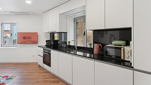 Une cuisine moderne avec des meubles blancs, un plan de travail noir, une machine à café, une bouilloire, un four à micro-ondes et un lave-vaisselle.