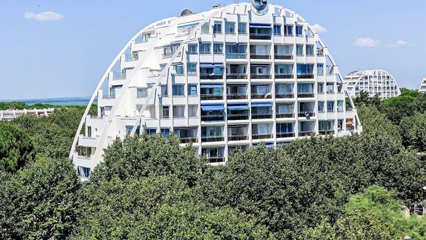Un bâtiment moderne à plusieurs étages, doté d’une architecture originale aux lignes courbes, et entouré d’une végétation luxuriante.