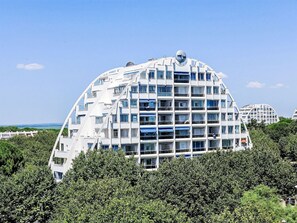 Un edificio moderno de varios pisos con una arquitectura curva distintiva, rodeado de abundante vegetación.