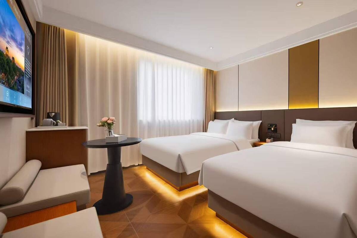 A hotel room with two beds, a desk, a chair, a TV, and a window with curtains.