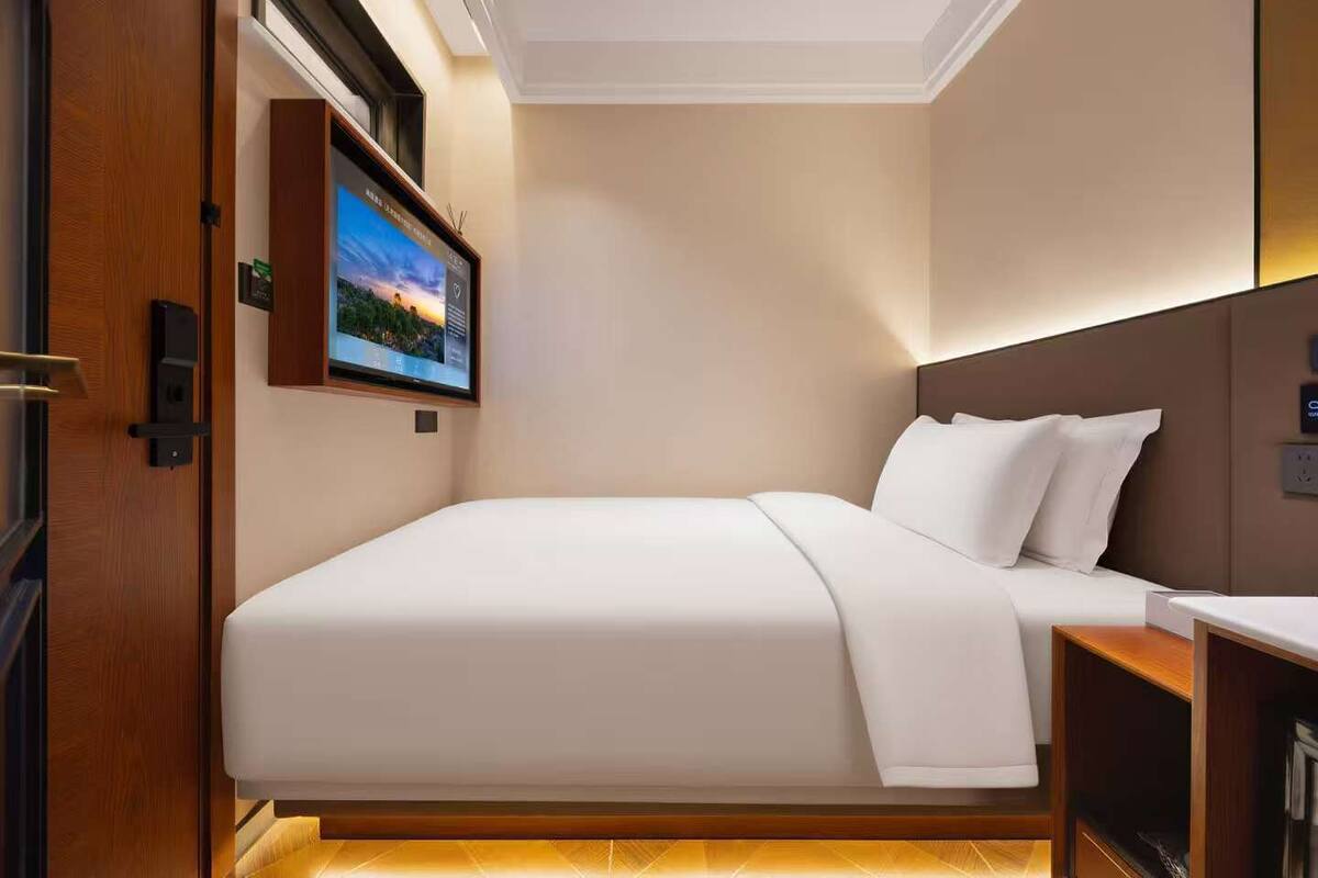 A hotel room with a bed, a TV mounted on the wall, and a wooden door.