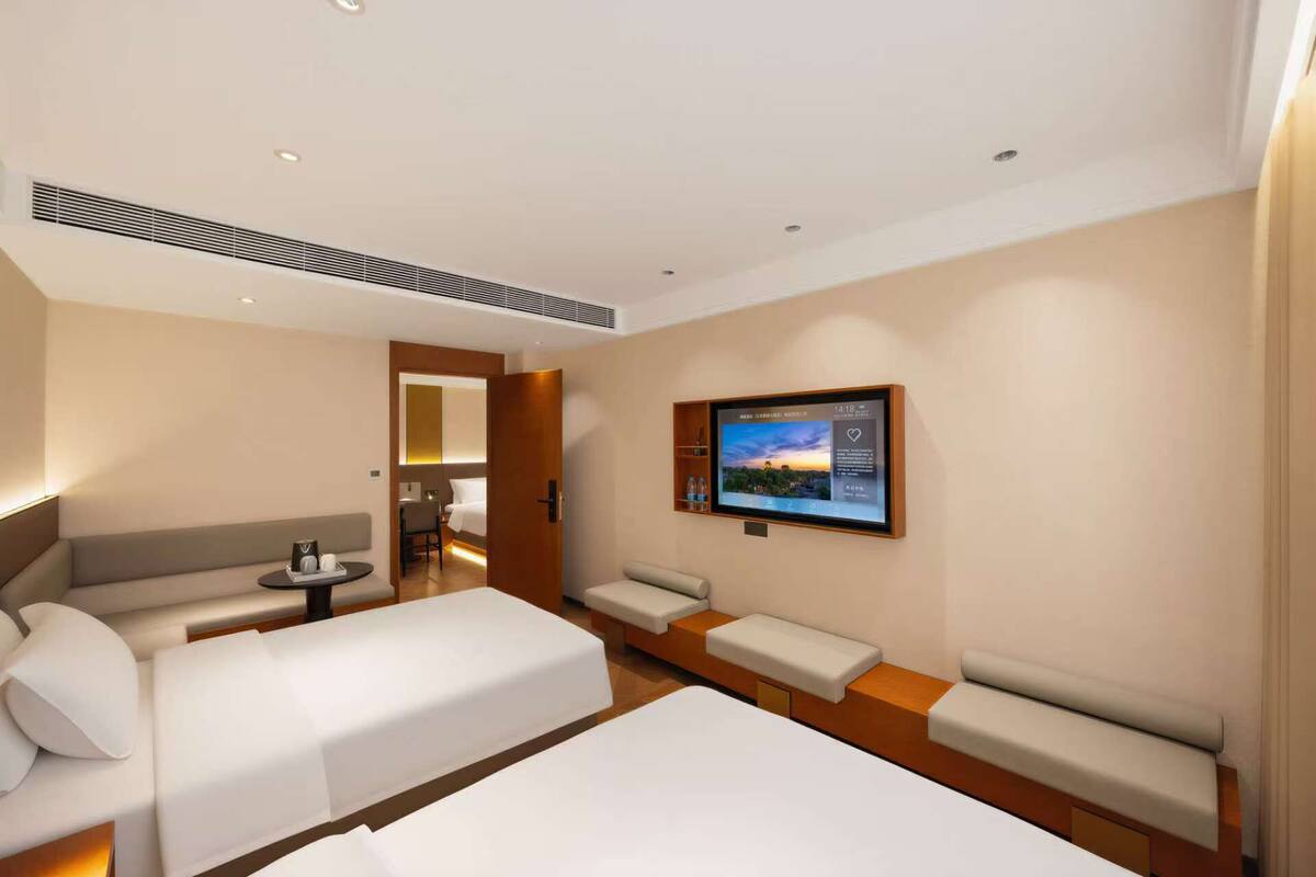 A hotel room with two beds, a sofa, a TV, and a desk.