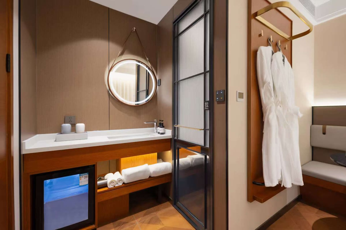 A modern bathroom with a wooden vanity, a round mirror, a towel rack, and a built-in television.