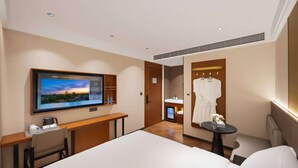 Een hotelkamer met een bed, een aan de muur bevestigde televisie, een bureau met stoel, een klein tafeltje met stoel en een badjas hangend aan de muur.