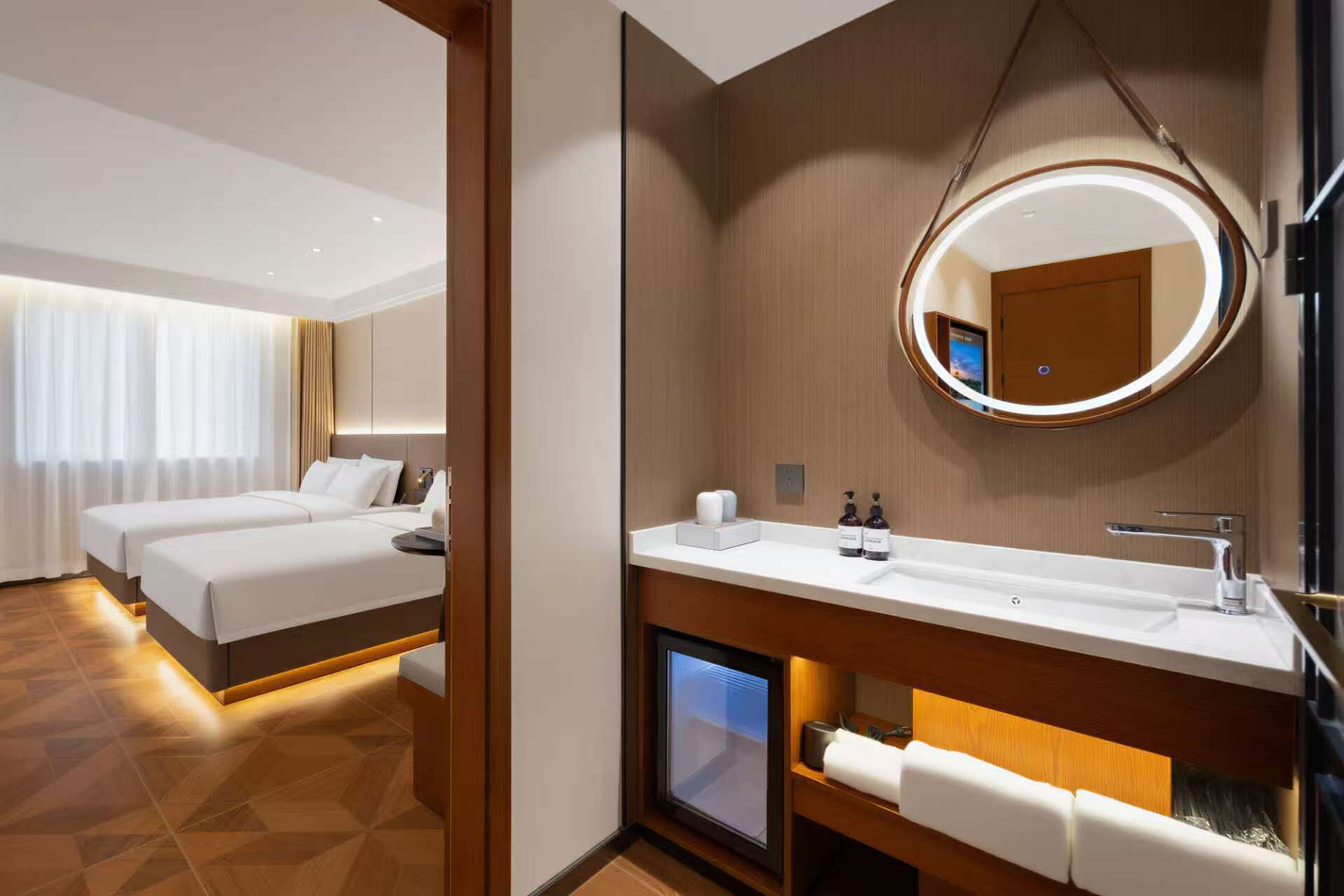 A hotel room with a bed, a bedside table, a mirror, a TV, and a bathroom with a sink and towel rack.