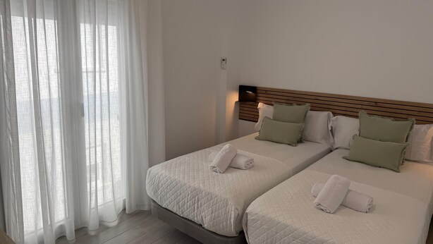 Quarto de hotel com duas camas, uma cabeceira de madeira e uma mesinha de cabeceira.