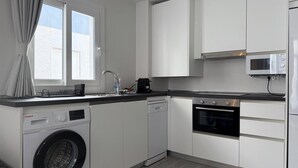 Cozinha moderna com armários brancos, máquina de lavar, lava-louças, fogão e micro-ondas.