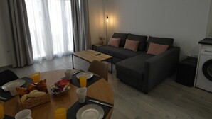 A modern living room with a sofa, a dining table set with breakfast items, and a washing machine. - ONE BEDROOM FLAT ...... (MALAGA)