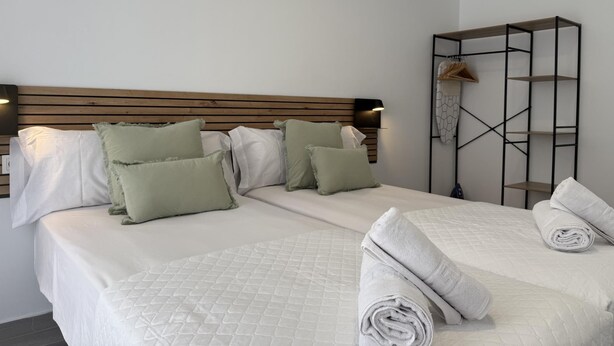 Una cama bien hecha con un edredón blanco acolchado, dos almohadas y una toalla blanca enrollada.