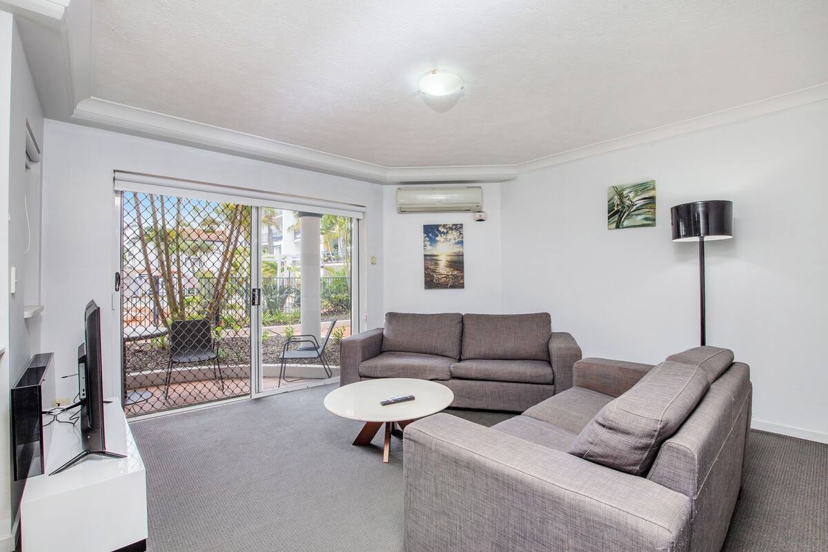A modern living room with a grey sofa, a white coffee table, and a TV on a stand.