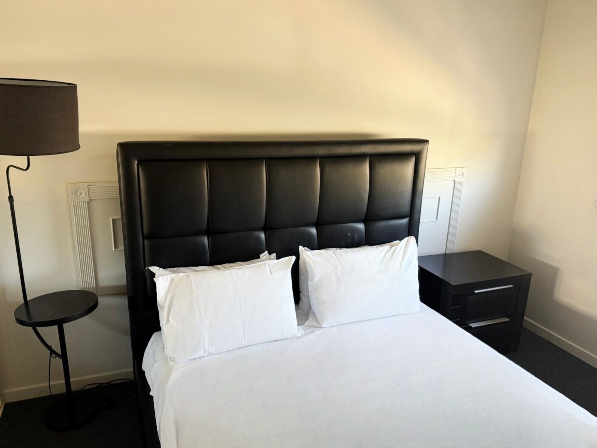 A hotel room with a large bed, two bedside tables, a floor lamp, and a radiator.