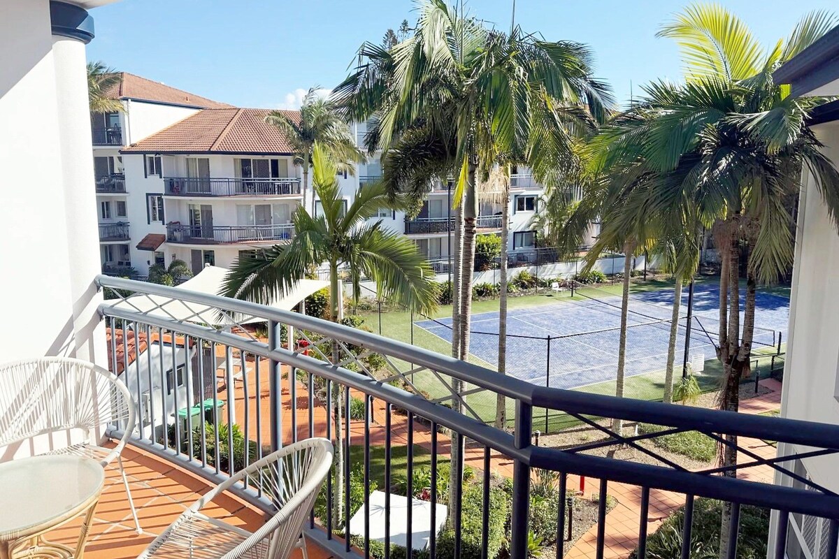 A balcony with a view of a pool, palm trees, and a building with balconies.