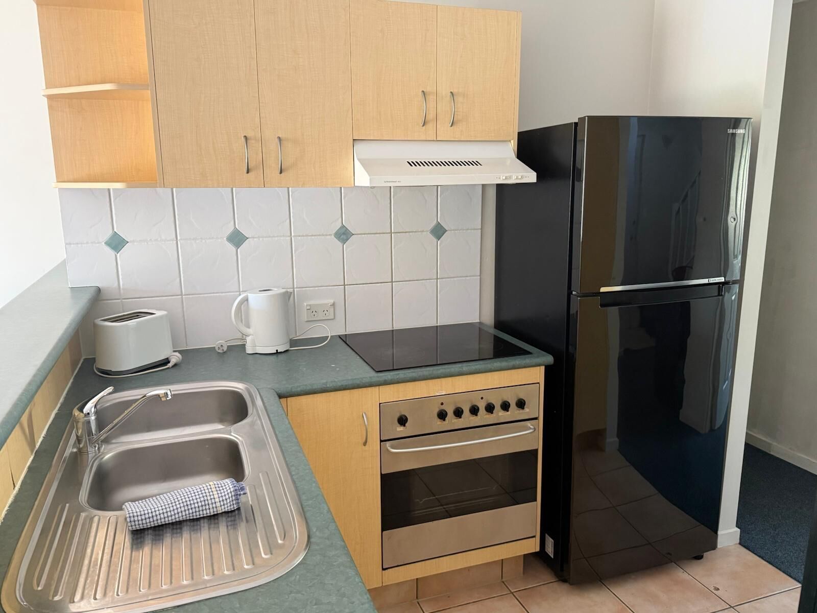 Una cocina compacta con un lavamanos, un tostador, una tetera, una estufa y un refrigerador negro.