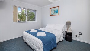 Una habitación de hotel con cama, ventana, un cuadro, lámpara y toma de corriente.
